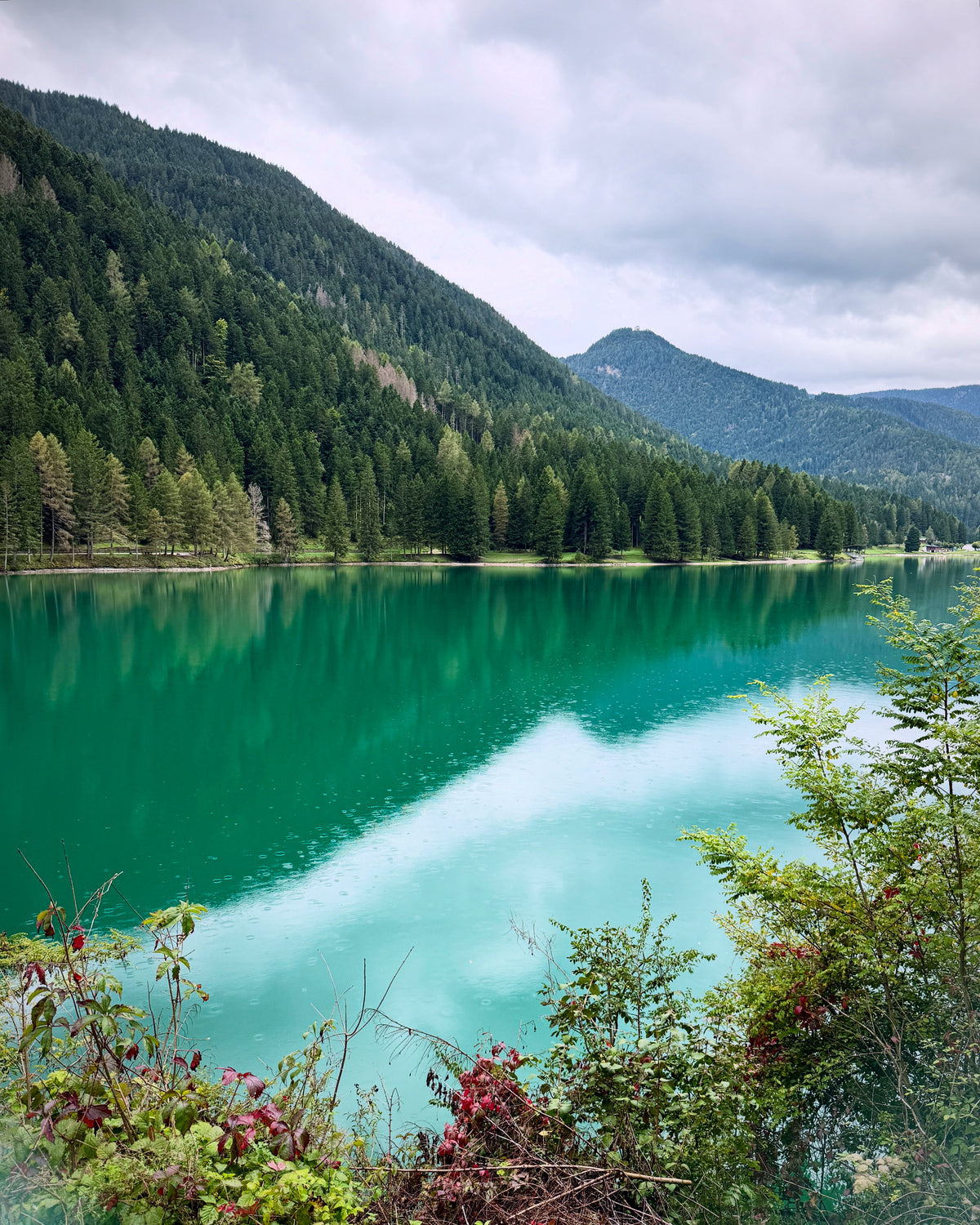 Turquoise mountain lake surrounded by forested slopes beneath a cloudy sky.