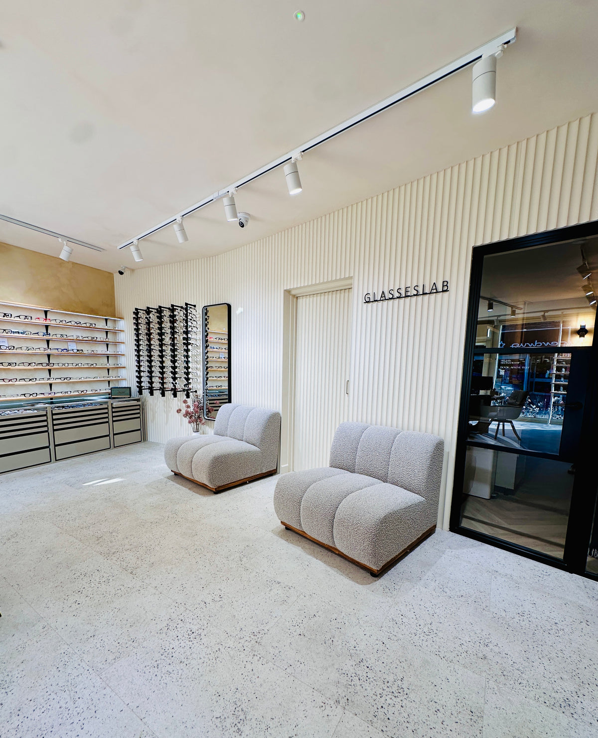Glasseslab Opticians interior with two upholstered chairs, a full-length mirror and wall-mounted eyewear displays.