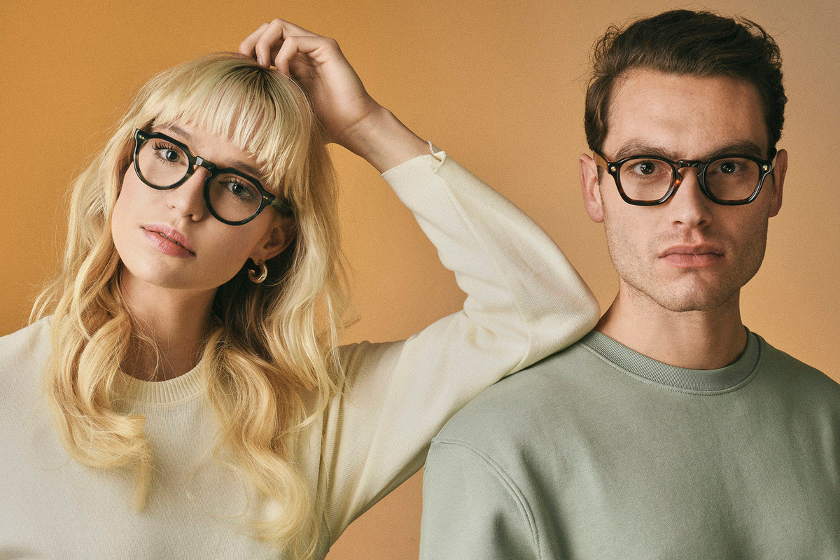 Two models wearing Cubo glasses against a warm tan background.