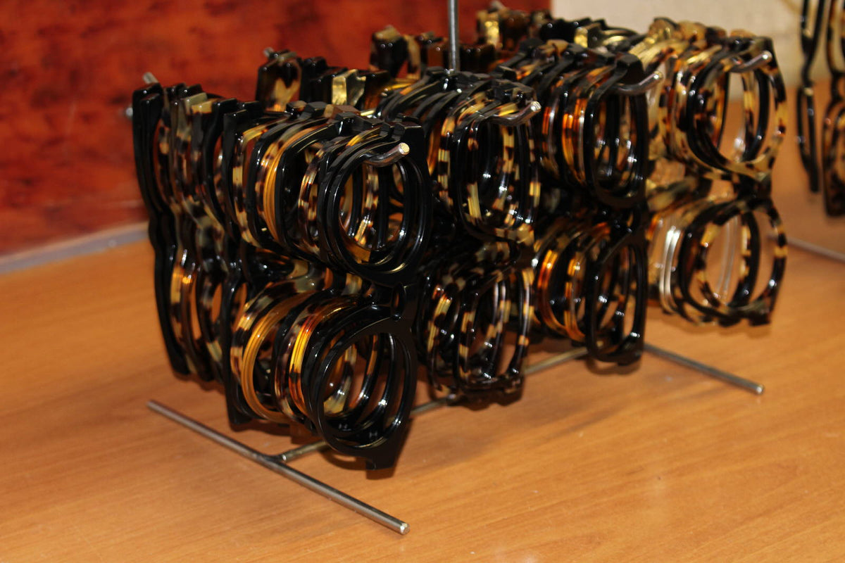 Black and tortoiseshell acetate frame fronts arranged on a rack in the eyewear workshop.