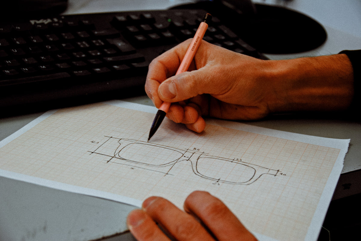 Designer drawing a spectacle frame and its measurements on graph paper.
