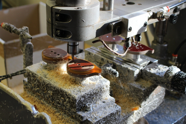 Eyewear workshop machine cutting acetate components, surrounded by pale material shavings.
